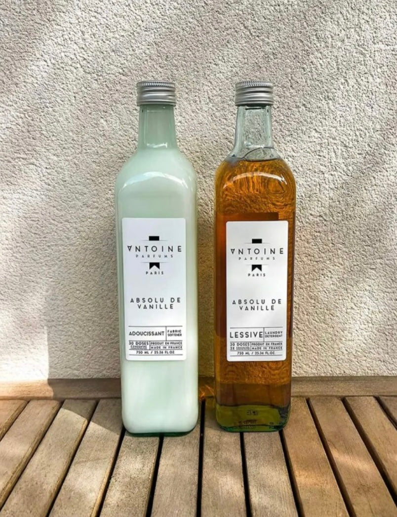 Two bottles of ANTOINE products on a wooden surface with a textured wall background.