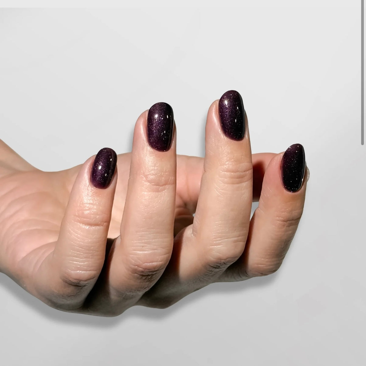 Hand with dark purple glittery nail polish on a light gray background