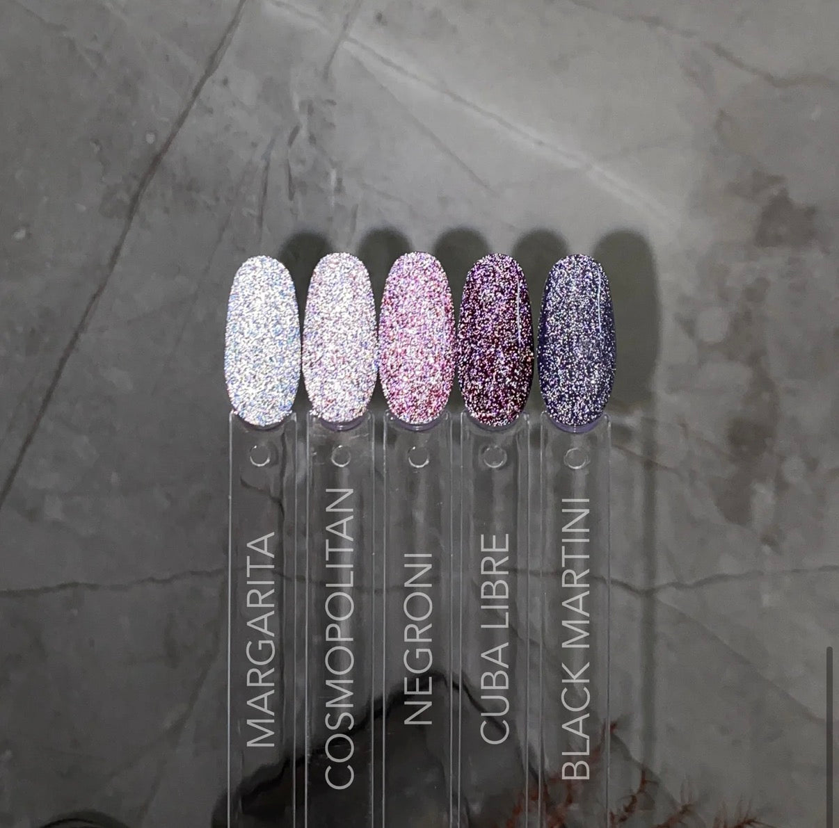 Set of five nail polish bottles with glittery finishes on a gray surface